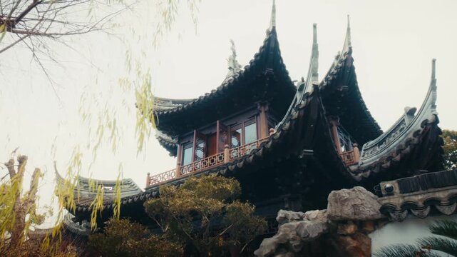 A close-up view of sweeping, upturned tiled rooflines on a traditional Chinese pavilion at Yuyuan Garden, Shanghai, framed by golden willow branches.