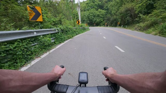 First-person POV footage of a road cyclist riding along a winding mountain road through lush tropical forest. The clip captures another cyclist approaching from the opposite direction, creating an aut
