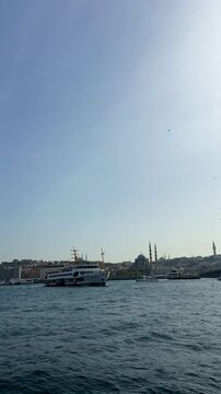 Istanbul, Turkey - April 20, 2025: Passenger ferry sails across Bosphorus with historic mosques, minarets and urban skyline in background, showing iconic waterfront cityscape.