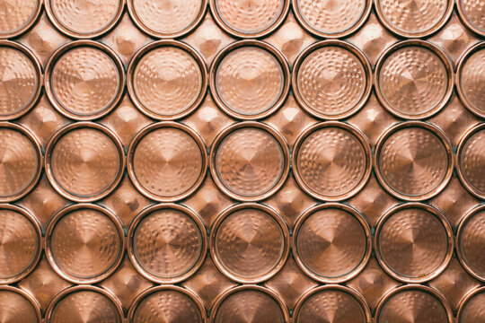 Close up of a metallic copper wall panel featuring a repeating pattern of circular discs with hammered and brushed radial textures