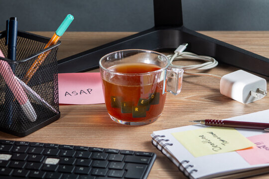 Exhausted and tired office worker need for caffeine. Keyboard keys dipped in coffee forming the word "tired" surrounded by urgent sticky notes. Concepts of work fatigue and morning grogginess