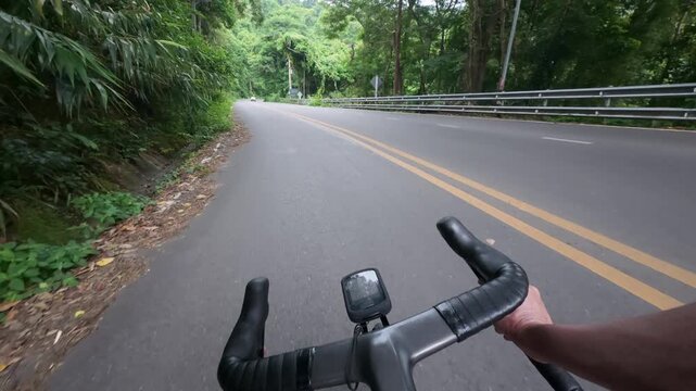 First-person POV footage of a road cyclist descending a scenic mountain road surrounded by lush tropical forest. A quiet roadway with light traffic, smooth asphalt, and immersive riding perspective ma