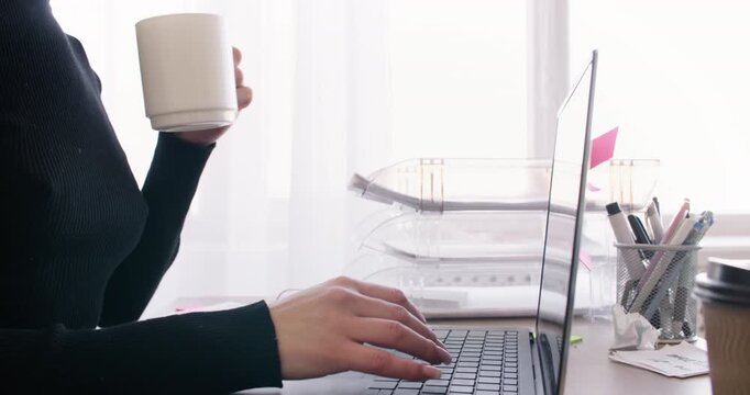 Office executive. Online job. Unrecognizable female manager working at desk typing on laptop drinking coffee at professional workplace.