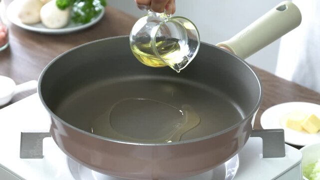 Fresh garlic cloves gently sizzling in a nonstick frying pan with a drizzle of cooking oil, preparing the perfect aromatic base for home cooking. Close-up shot in a bright modern kitchen with natural 