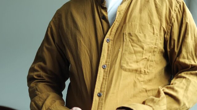 Horizontal 4K close up shot of a man hands buttoning his mustard yellow casual shirt from top to bottom