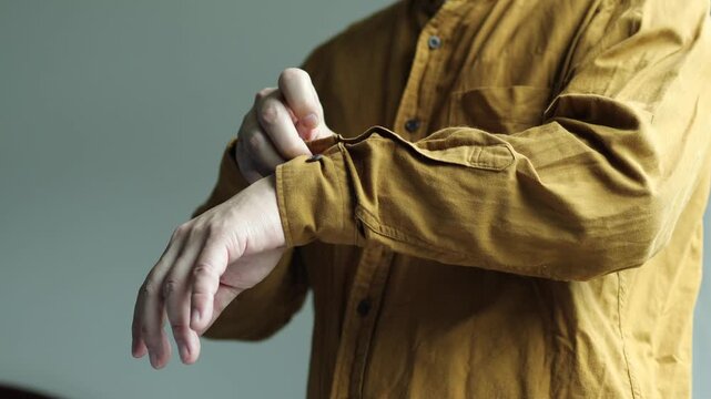 Horizontal 4K video showing a man using his right fingers to fasten the wrist cuff button on his left long sleeve shirt