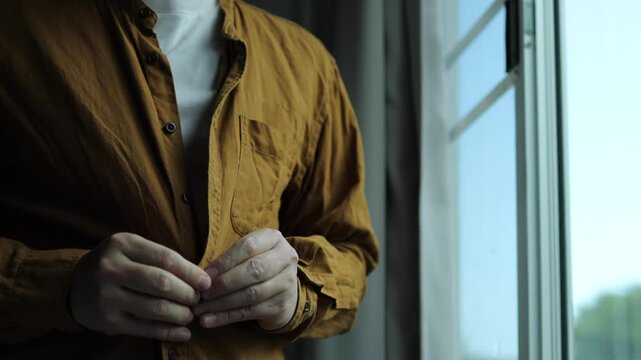 Horizontal 4K close up video of a man unbuttoning his mustard yellow shirt and taking it off leaving only his white t-shirt