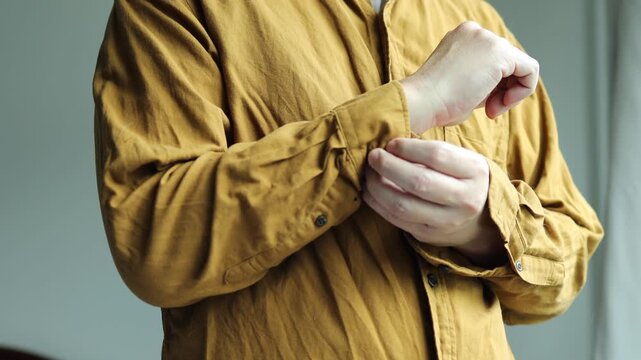 Horizontal 4K video showing a man using his left fingers to fasten the wrist button on his right shirt sleeve cuff