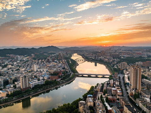 Aerial perspective of a city with a winding river, multiple bridges, and distant mountains during a vibrant sunset.