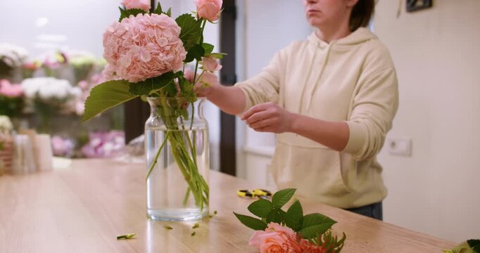 Fresh bouquet. Flower decoration. Woman florist creating blossom composition in glass vase trimming carnation stems in home atmosphere.