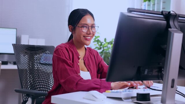Woman office computer desk eyeglass smile business workplace professional technology employee worker keyboard monitor workstation chair screen mouse indoor happy applauding red shirt