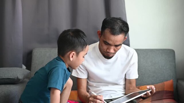 Father and son Magnetic Drawing Board spend time drawing together on the sofa with happiness.