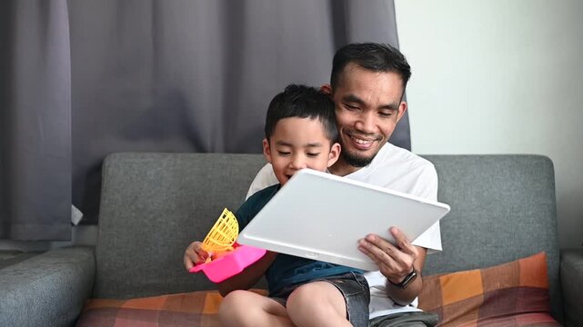 Father and son Magnetic Drawing Board spend time drawing together on the sofa with happiness.