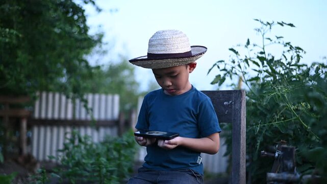 4 Year Old ASEAN Boy Using Tablet in Vegetable Garden Exploring Smart Farming AI Technology and Future Food Security Concept