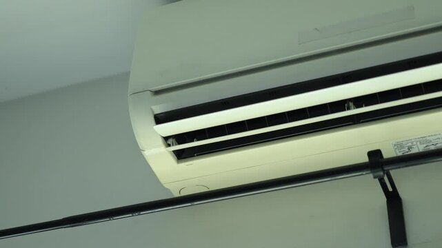 Horizontal 4K video of a wall mounted indoor air conditioner unit adjusting its flap louver direction up and down after receiving remote command