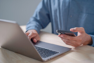 Fototapeta premium Close Up of Person Using Smartphone While Working on Laptop, Remote Work, Business Technology, Digital Communication, and Productivity Concept