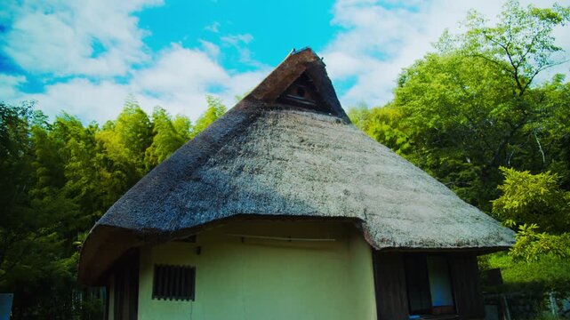 青空と竹林に映える茅葺き屋根と土壁の伝統的な日本古民家 4Kシネマティック映像素材