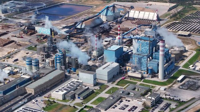 Aerial perspective of a large pulp mill and biomass power plant processing wood into cellulose. Industrial chimneys releasing steam