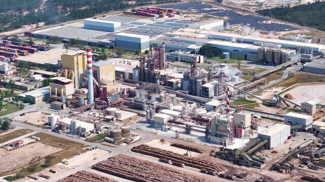 Expansive aerial view of a pulp and paper mill with its processing facilities, smokestacks, and large raw material yards for biomass energy