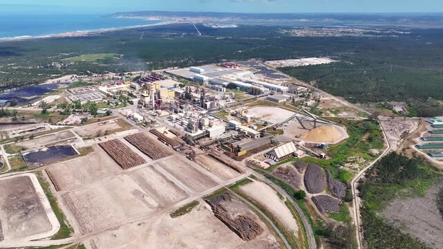 Industrial pulp and paper mill aerial view showing wood processing, biomass piles, and the factory complex. Sustainable bioenergy production