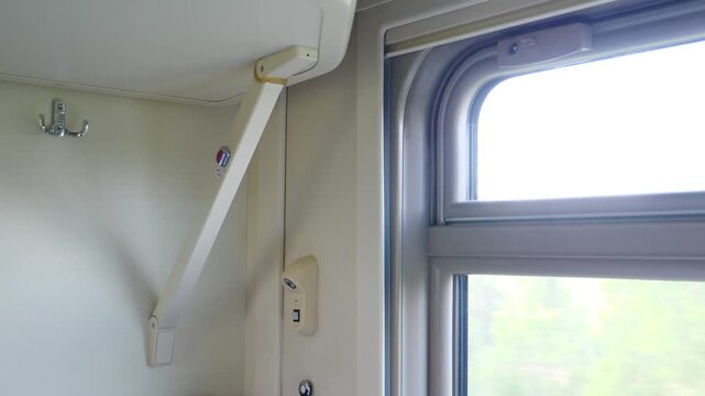 Interior of a Russian train compartment showing a white fold-down shelf with a metal bracket, a coat hook, and a window with a blurred green landscape outside 4k video