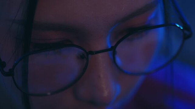 Eyeglasses on woman face close up eye portrait with blue light dark reflection, intimate low key mood, lens glow, skin detail, calm quiet atmosphere