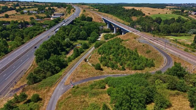 LArmoricaine D31 crosses above the Paris Brest railway near Change, Mayenne, Pays de la Loire, France, linking major transport corridors through woodland and farmland, drone forward flyover.