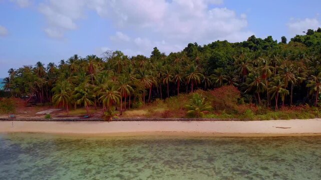 Sliding shot past a bangka boat moored along a sandy beach backed by dense coconut palms and a nipa hut with turquoise ocean visible beyond the tree line