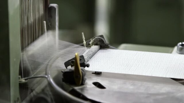 Close-up of an automated industrial loom weaving technical medical fabric inside a modern manufacturing facility. High-speed textile production process for healthcare applications.
