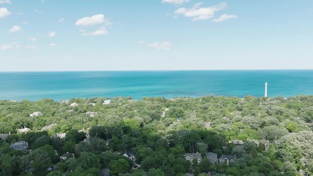 Aerial flyover glides over wealthy Winnetka Illinois homes hidden among trees with cloud shadow moving across canopy, lighthouse and Lake Michigan beyond