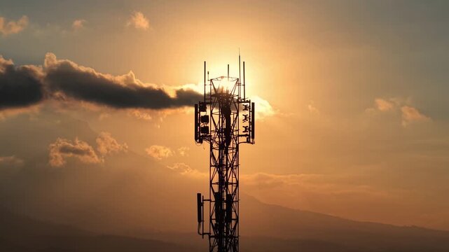 Silhouette of cellular tower against golden sunset sky. Telecommunication, network, and technology concept, dramatic evening cloudy background footage.