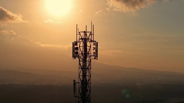 Cell tower silhouette against vibrant sunset sky and clouds. Telecommunication infrastructure, network signal, and technology concept footage.