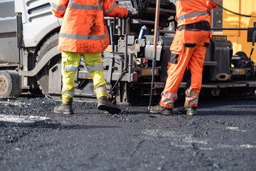 Construction workers repair a road using machinery in a busy urban setting during the day
