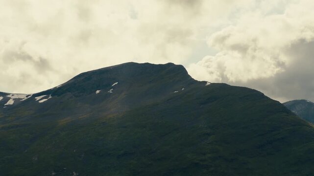Gentle daylight grazes the sloping Bl&aring;hornet summit as patchy late snow lingers beneath a thick cloud deck in Sunnm&oslash;re.