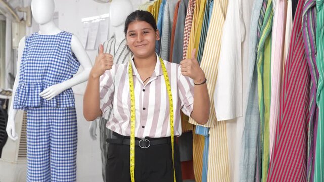 Successful indian Gen Z female small business owner do thumbs up in her garment and clothing textile design studio workshop. Woman Fashion designer or dressmaker. Tailor industry. Skill india