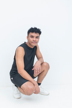 A young filipino male in athletic wear holds a squatting pose while looking directly at the camera in a isolated white background..
