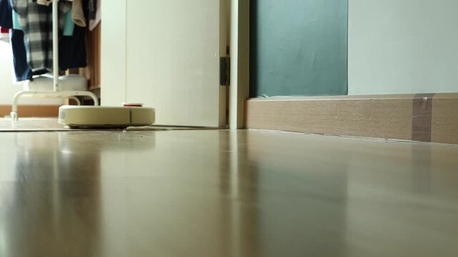 Horizontal 4K video with camera panning to track a white smart robot vacuum cleaner moving back and forth across a bedroom door threshold