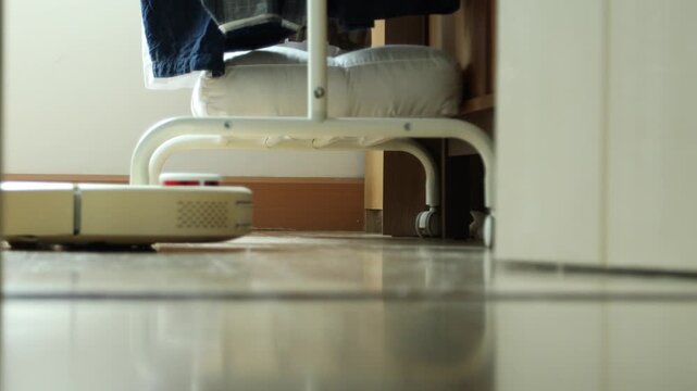 Horizontal 4K ground level close up showing fine dust particles on parquet floor as a white robot vacuum cleaner approaches from bedroom
