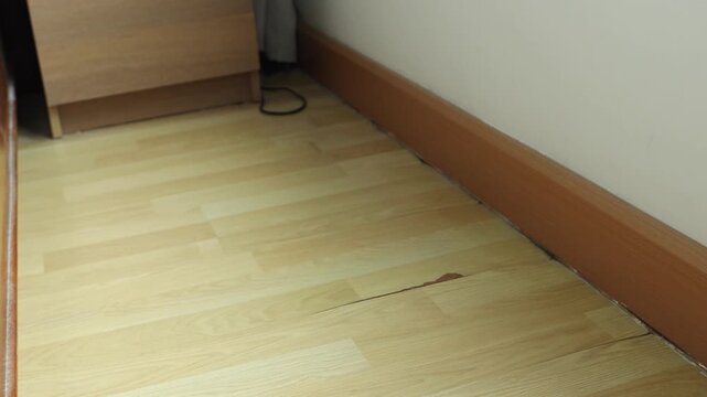 Horizontal 4K video of a white automatic robot vacuum cleaner navigating through a narrow walkway gap between a wall and bed frame
