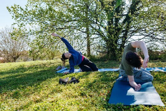 two friends doing yoga stretches outdoors in a park