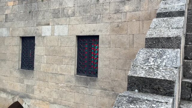 Ancient stone wall with arched windows and medieval staircase in architectural landscape.