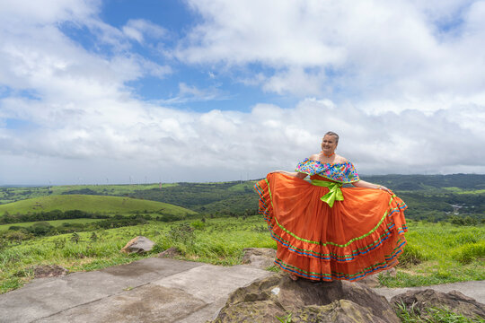 Woman in traditional pollera dress standing on green hills
