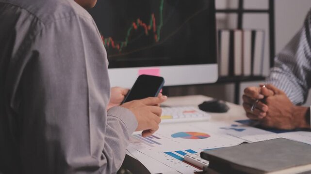 Two busy business men investors doing financial trading market data analysis. Male advisor and analyst consulting about stock exchange investing pointing at chart on laptop computer working in office.