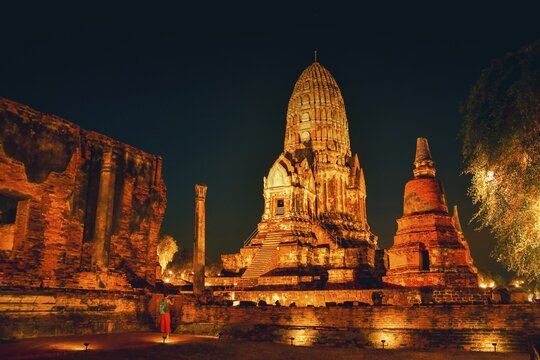 Visitor taking picture Wat Ratchaburana ancient temple in Ayutthaya. Illuminated central prang ruins. Purple twilight blue hour sky. Siam kingdom preserved ancient ruins. Unesco world heritage site