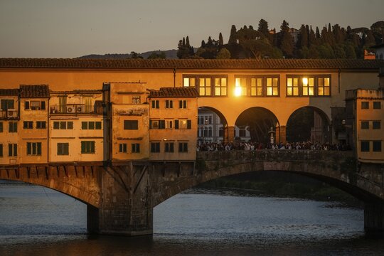 Warm evening light falls on the historic Ponte Vecchio segmental arch bridge across the Arno River and is reflected in window panes, evening mood, old town, Florence, Tuscany, Italy