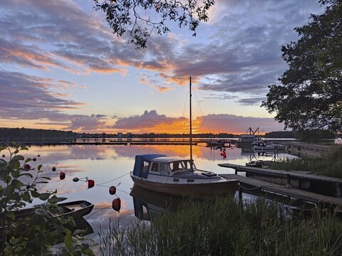 A boat is moored on a jetty in a calm lake at sunset with glowing clouds and reflections in the water, G&ouml;ta Canal, Karlsborg, V&auml;stra G&ouml;talands l&auml;n, Sweden