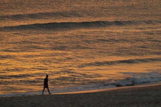 Walkers on the beach, setting sun colors the sea and waves golden, Houvig Beach, North Sea, Denmark