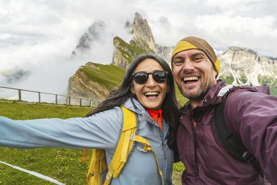 Cheerful couple of hikers friends taking selfie in Dolomites mountains.Millennial guy girl enjoying summertime day out trip laughing at camera together - Millennial travelers standing in scenic nature