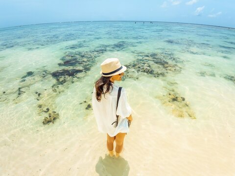 Tourist Woman on vacation standing at shoreline facing turquoise Indian Ocean on Zanzibar south coast tropical travel lifestyle scene Tanzania