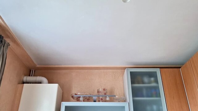 Bright apartment kitchen corner with wooden cabinets, white ceiling, ventilation duct, and glass front storage. Clean residential interior showcasing practical home design and everyday living